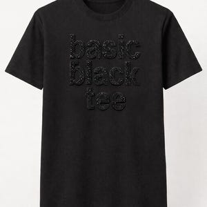 May include: A black t-shirt with the words "basic black tee" spelled out in small, sparkling, dark-colored embellishments. The shirt has short sleeves and a crew neck.