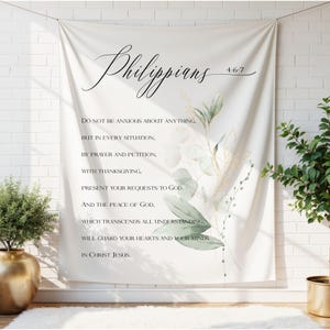May include: Cream-coloured wall hanging with the word "Philippians" in cursive, and verses 4:6-7. It features green and gold botanical illustrations. The text reads: "Do not be anxious about anything..." and continues with the full verse.