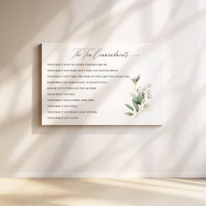 May include: A rectangular canvas print featuring "The Ten Commandments" in elegant script. The text is arranged in a vertical list. A watercolor floral design with green leaves and gold accents adorns the right side, adding a touch of natural beauty.