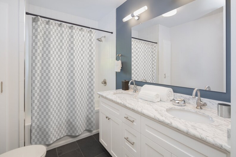 May include: A white bathroom vanity with a marble countertop and two sinks. The vanity has two drawers and two doors. There is a shower curtain behind the vanity.
