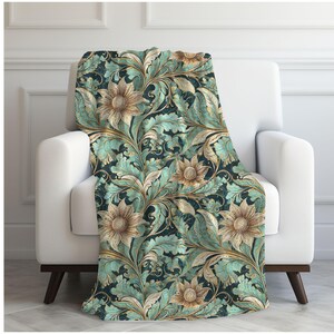 May include: A teal and gold floral throw blanket with a repeating pattern of stylized flowers and leaves. The blanket is draped over a white armchair.