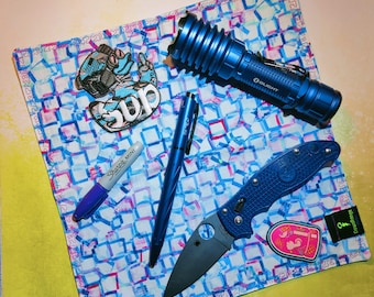 May include: A blue and white patterned bandana with a blue flashlight, a blue pocket knife, a blue Sharpie marker, and a blue and white sticker with the word "Sup" on it.