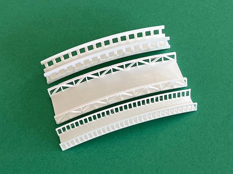 May include: Three white plastic model bridges with different designs. The top bridge has a simple railing, the middle bridge has a lattice design, and the bottom bridge has a more detailed railing.