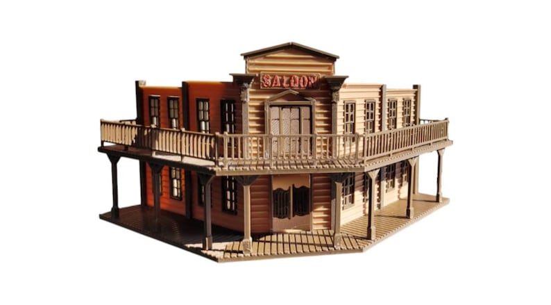 Pode incluir: Um modelo de saloon de madeira em miniatura com uma varanda e a palavra "SALOON" acima da entrada. O edif&iacute;cio tem uma apar&ecirc;ncia r&uacute;stica e desgastada com tons de castanho e bege, evocando um tema do Velho Oeste.