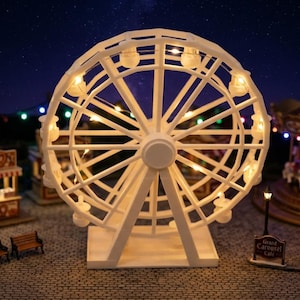 May include: A white miniature Ferris wheel model featuring a circular frame with spokes and attached passenger gondolas. The structure is illuminated by warm yellow string lights woven through the frame, set against a dark night sky background.