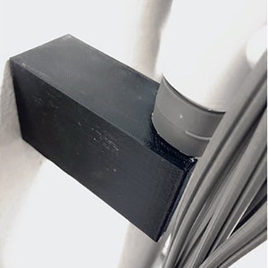 May include: A black 3D printed cable management organizer attached to a white pole with a gray base. The organizer is designed to hold and organize cables.