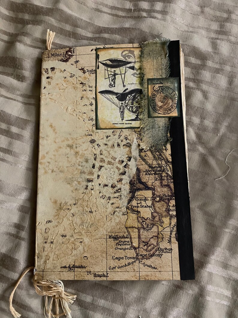 May include: A vintage-style journal with a brown leather cover and a map of Africa on the front. The journal has a black spine and a frayed fabric edge. The map includes the text "Cape Town", "Cape Colony", "Walfischbai", "Orange R", "Agulhas", "Cof Good Hope", and "Aurban Natal".