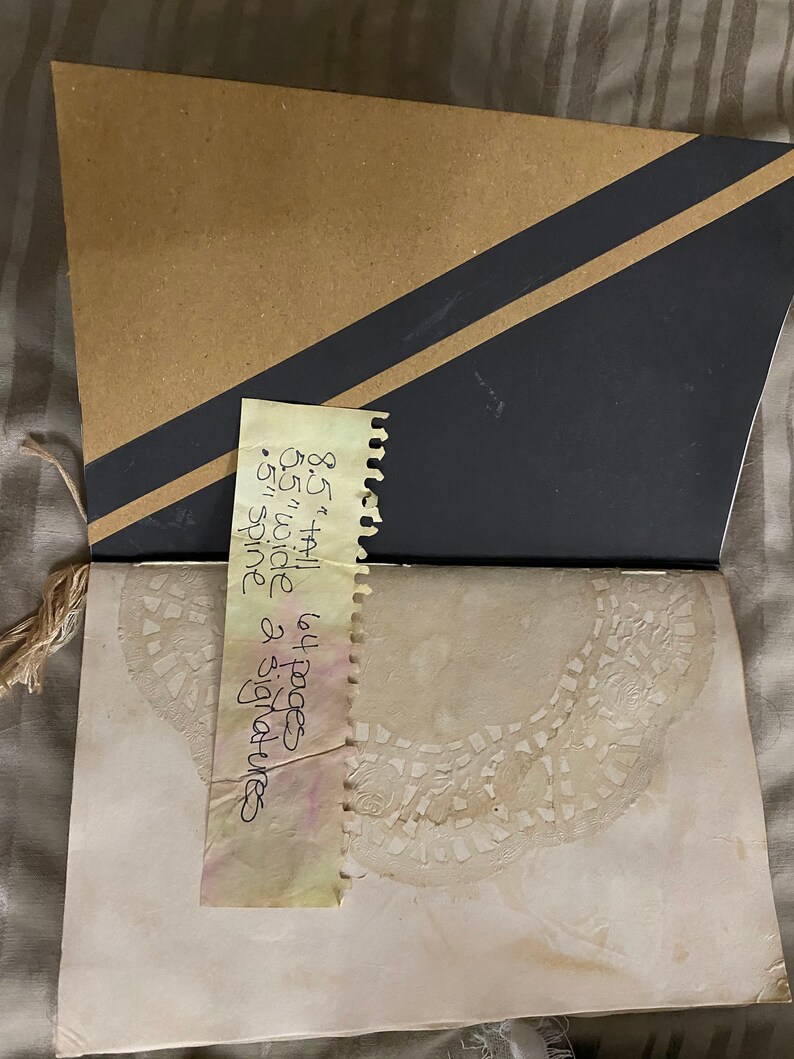 May include: A brown paper notebook with a black and brown striped cover. The notebook is open to a page with a lace design. A yellow note is attached to the cover with the text: "8 1/2 x 11 64 pages 65 wide spine & signatures".