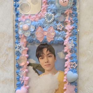 May include: Clear phone case decorated with blue and pink frosting-like embellishments, a photo of a person, and various charms including a bear, stars, and hearts. The word "SEVENTEEN" is spelled out at the bottom.