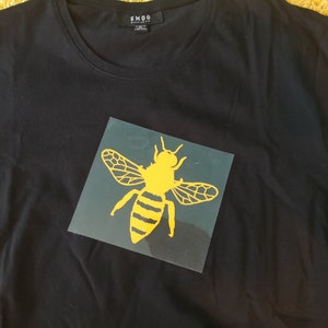 Peut inclure: Un t-shirt noir avec un motif de silhouette d'abeille jaune.