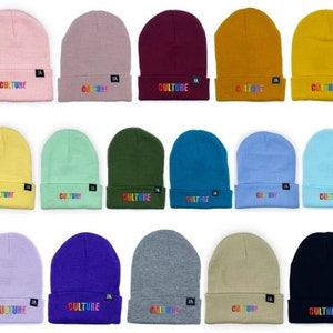 May include: A selection of beanies in a range of colours, such as pink, grey, and navy. Each beanie displays the word "CULTURE" in rainbow text on the folded brim. A small black tag is present on each beanie.