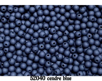 May include: A collection of matte, round, blue beads with a hole through the center. The beads are a dusty blue color. The text "52040 cendre blue" is at the bottom of the image.