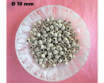 May include: A clear glass bowl filled with numerous light-colored wooden beads, each approximately 10 mm in diameter. The bowl sits on a pink surface. The beads are round with a hole through the center, suitable for stringing.