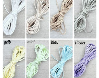 May include: A collection of eight coiled cords in various colors including white, beige, champagne, olive, yellow, mint, blue, and lilac. Each cord is neatly bundled and labeled with its corresponding color name in German text above the coil.