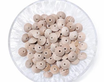 May include: A collection of unfinished wooden beads with a central hole, displayed in a white, textured bowl. The beads are light brown and round, perfect for crafting and jewelry making. The bowl has a pearlescent, marbled appearance.