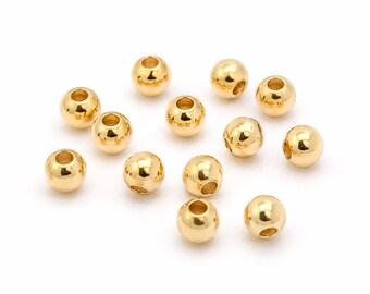 May include: A collection of twelve small, spherical, metallic gold-toned beads. Each bead features a smooth, reflective surface and a central hole, designed for stringing. The beads are arranged in a loose, scattered formation on a plain surface.
