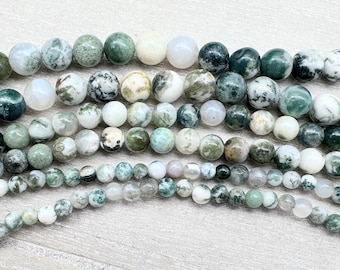 May include: Strands of round gemstone beads in various sizes and shades of green, white, and gray. The beads have a mottled appearance, with some displaying a mossy green pattern. The beads are strung together, ready for jewelry making.