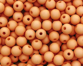 May include: A close-up shot of a pile of light orange wooden beads. Each bead is round with a hole drilled through the center. The beads are scattered, creating a textured surface.