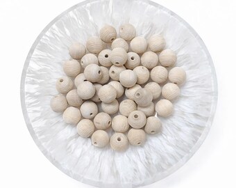 May include: A collection of light-colored wooden beads with a grooved texture, displayed in a clear, round, decorative bowl with a white, marbled design. The beads are spherical and have a hole through the center.
