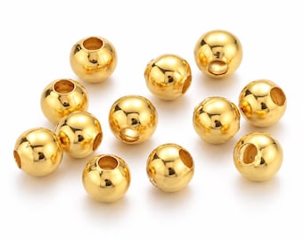 May include: A collection of eleven spherical beads with a polished gold-tone finish. Each bead features a smooth, reflective surface and a central hole for threading, arranged in a scattered formation on a plain white background.