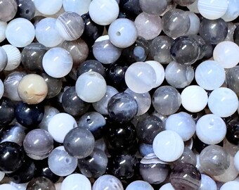 May include: A collection of round beads in various shades of gray, white, and black. The beads have a polished, smooth surface and are of varying sizes. Some beads have a marbled appearance, while others are solid in color. The beads are likely for jewelry making.