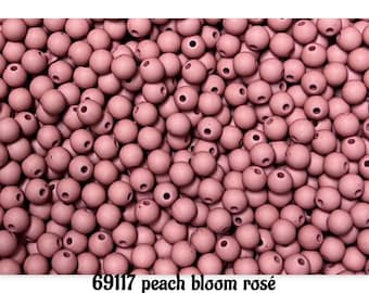 May include: A collection of round, matte-finish beads in a solid dusty peach-pink color. Each bead features a centered hole for threading. The text 69117 peach bloom rosé is printed in black at the bottom of the image frame.