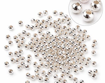 May include: A large collection of small, round, metallic silver beads scattered across the surface. Each bead features a smooth, reflective finish and a central hole for threading. A circular inset shows a magnified view of four beads.