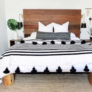 May include: A white and black striped bedspread with black pom-poms along the bottom edge. The bedspread is on a bed with a wooden headboard and white pillows.