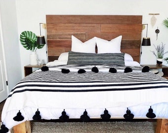 May include: A white and black striped bedspread with black pom-poms along the bottom edge. The bedspread is on a bed with a wooden headboard and white pillows.