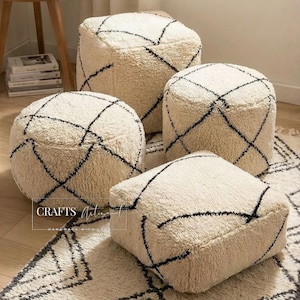 May include: Four cream-colored, textured poufs with black geometric designs. The poufs are arranged on a matching rug, creating a cohesive and stylish seating arrangement. The poufs are various shapes and sizes.