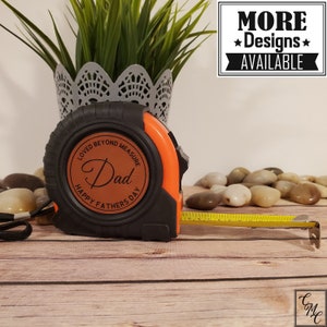 May include: A black and orange tape measure with a brown leather circle that says "Loved Beyond Measure Dad Happy Father's Day".