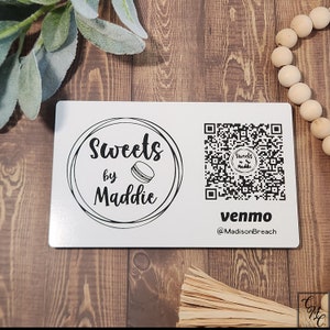 May include: A white business card with a black logo that says "Sweets by Maddie" and a macaron graphic. The card also has a black and white QR code and the text "venmo @MadisonBreach".