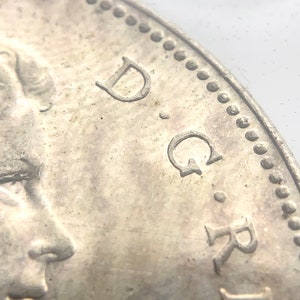 May include: Close-up of a silver coin featuring a portrait of a woman on the left and the letters "D.G.R." on the right.
