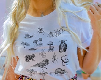 May include: White t-shirt with a black and white graphic print of various insects, animals, and plants. The graphic includes a snail, beetle, bat, dragonfly, mushroom, frog, crow, spider, snake, bee, and rat.