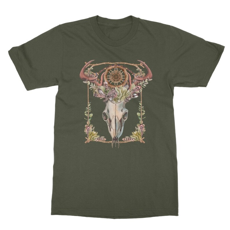 May include: Olive green t-shirt featuring a watercolor design of a skull with antlers, a dreamcatcher, and floral accents. The design is framed with a gold border and botanical elements. The shirt is a classic crew neck style.