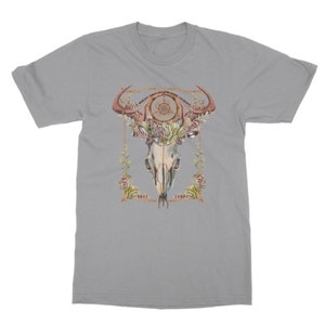 May include: A light gray t-shirt featuring a watercolor design of a bull skull with antlers, a dreamcatcher, and floral accents. The design is framed with a gold-colored border. The shirt is a crew neck style.