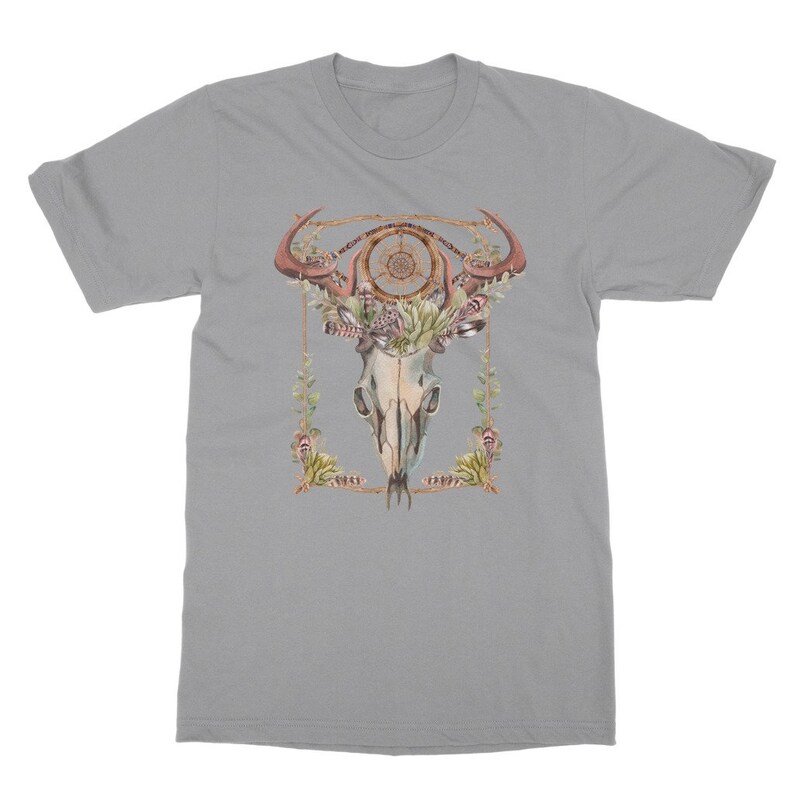 May include: A light gray t-shirt featuring a watercolor design of a bull skull with antlers, a dreamcatcher, and floral accents. The design is framed with a gold-colored border. The shirt is a crew neck style.