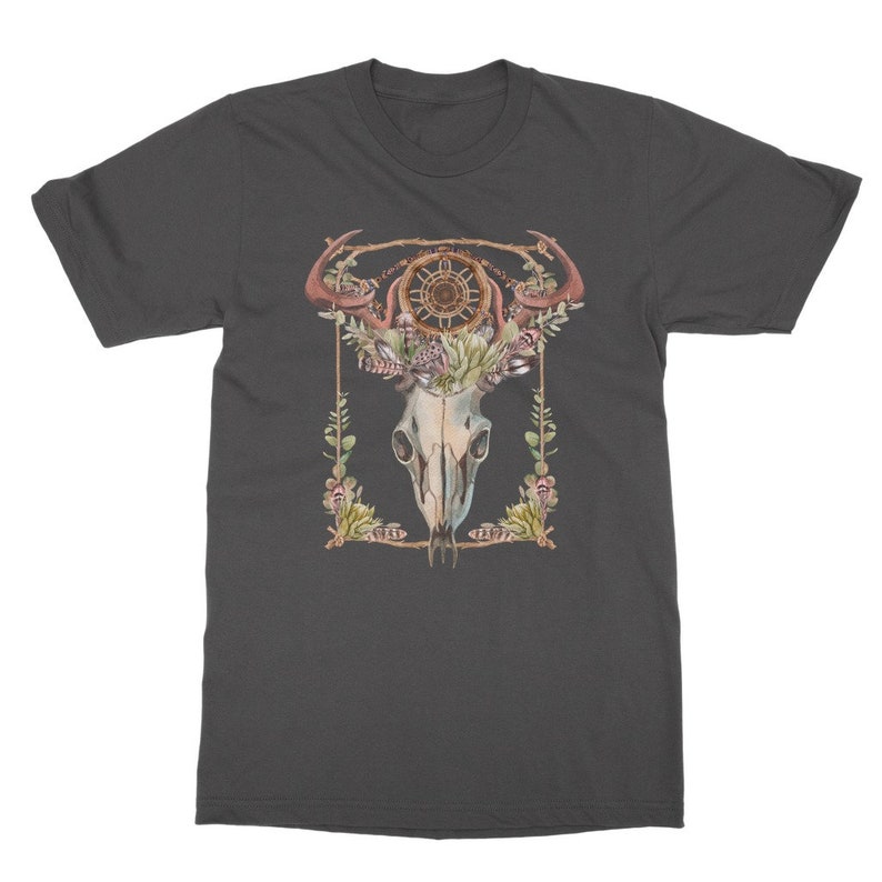 May include: Dark gray t-shirt featuring a watercolor design of a skull with antlers, a dreamcatcher, and floral elements. The design is framed with a gold border and green foliage. A unique graphic tee.