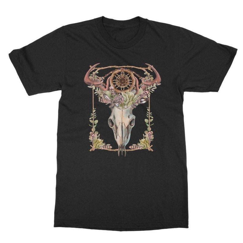 May include: Black t-shirt featuring a watercolor design of a skull with antlers, a dreamcatcher, and floral accents. The design is framed with a gold border. The shirt is a classic crew neck style.