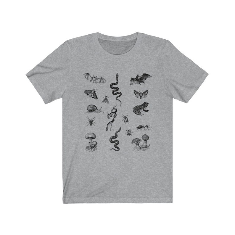 May include: A heather gray t-shirt featuring a detailed black and white illustration of various insects, amphibians, and fungi. The design includes bats, snakes, moths, a frog, a snail, and mushrooms. The shirt has a crew neck and short sleeves.