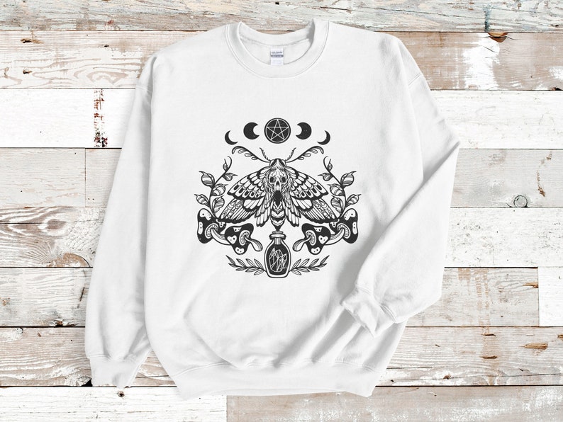 May include: White sweatshirt with a black and white graphic print of a moth, a pentagram, moons, and a bottle. The graphic is centered on the front of the sweatshirt.