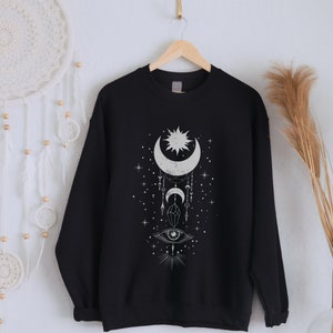 May include: Black sweatshirt with a white graphic design of a crescent moon, sun, and eye with stars and geometric shapes.