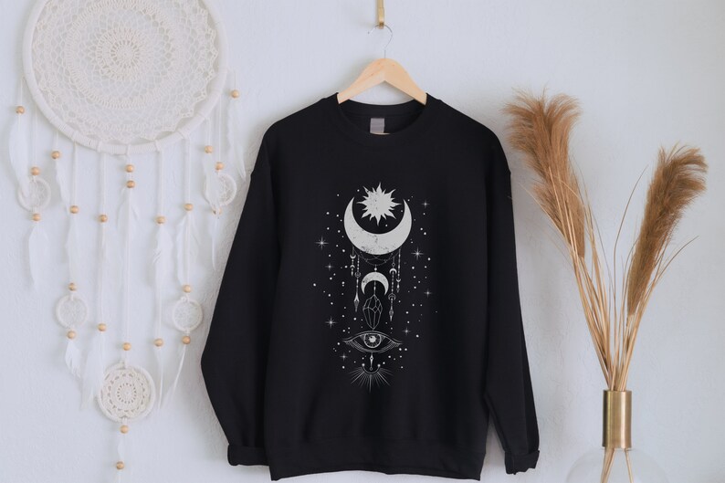 May include: Black sweatshirt with a white graphic design of a crescent moon, sun, and eye with stars and geometric shapes.