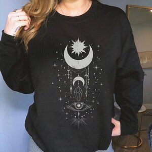 May include: Black sweatshirt with a white graphic design featuring a crescent moon, sun, stars, a crystal, and an eye.