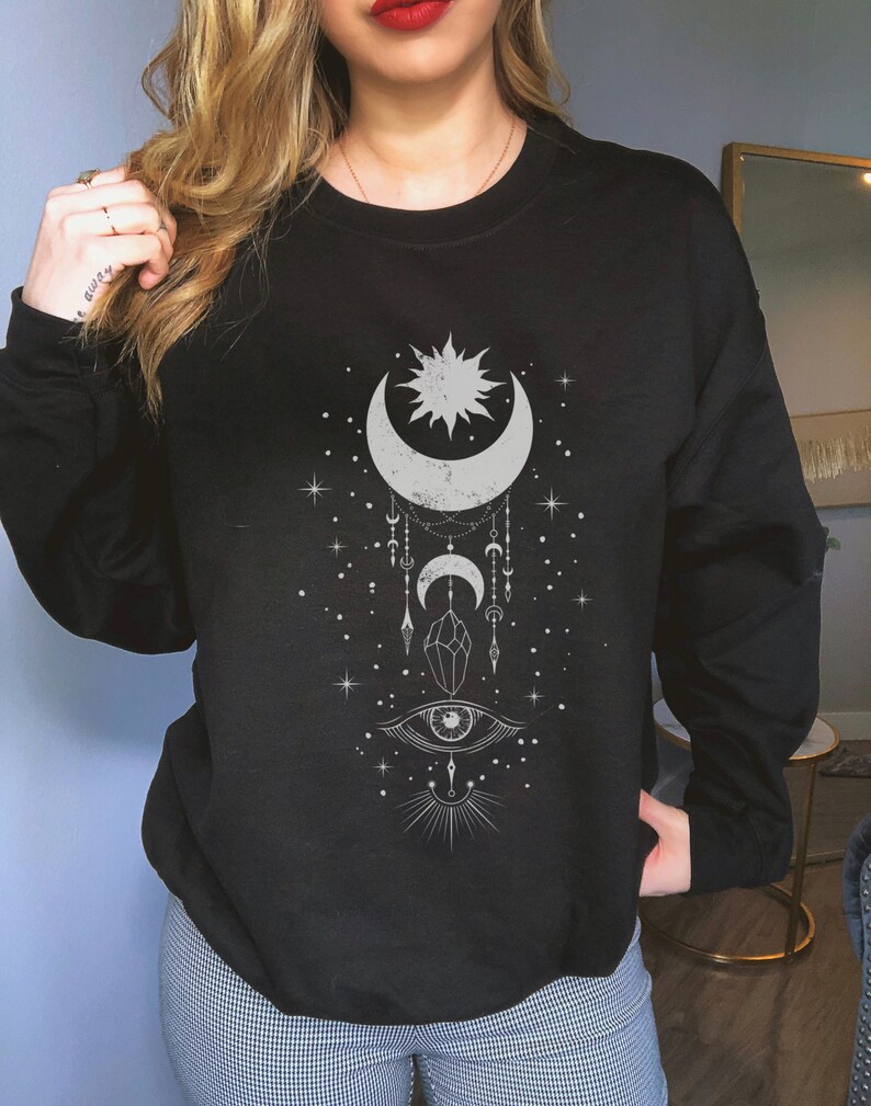 May include: Black sweatshirt with a white graphic design featuring a crescent moon, sun, stars, a crystal, and an eye.