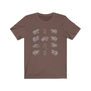 Pode incluir: Uma camiseta marrom com um design branco de v&aacute;rios sapos e girinos. O design &eacute; repetido em toda a camiseta.