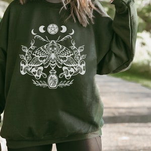 May include: A dark green sweatshirt with a white graphic print of a moth, a pentagram, and crescent moons. The moth is surrounded by leaves and mushrooms.