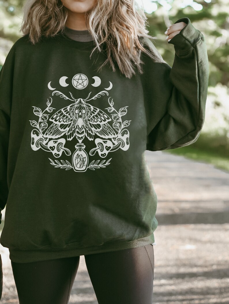 May include: A dark green sweatshirt with a white graphic print of a moth, a pentagram, and crescent moons. The moth is surrounded by leaves and mushrooms.