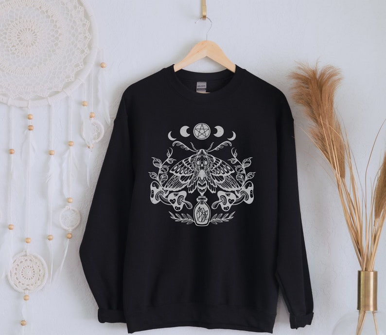 May include: Black sweatshirt with a white graphic print of a moth, a pentagram, and three crescent moons. The moth has a skull and crossbones design.