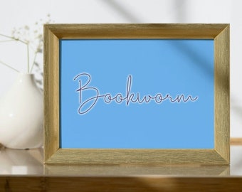 May include: A gold-framed picture with a light blue background and the word "Bookworm" written in purple cursive.